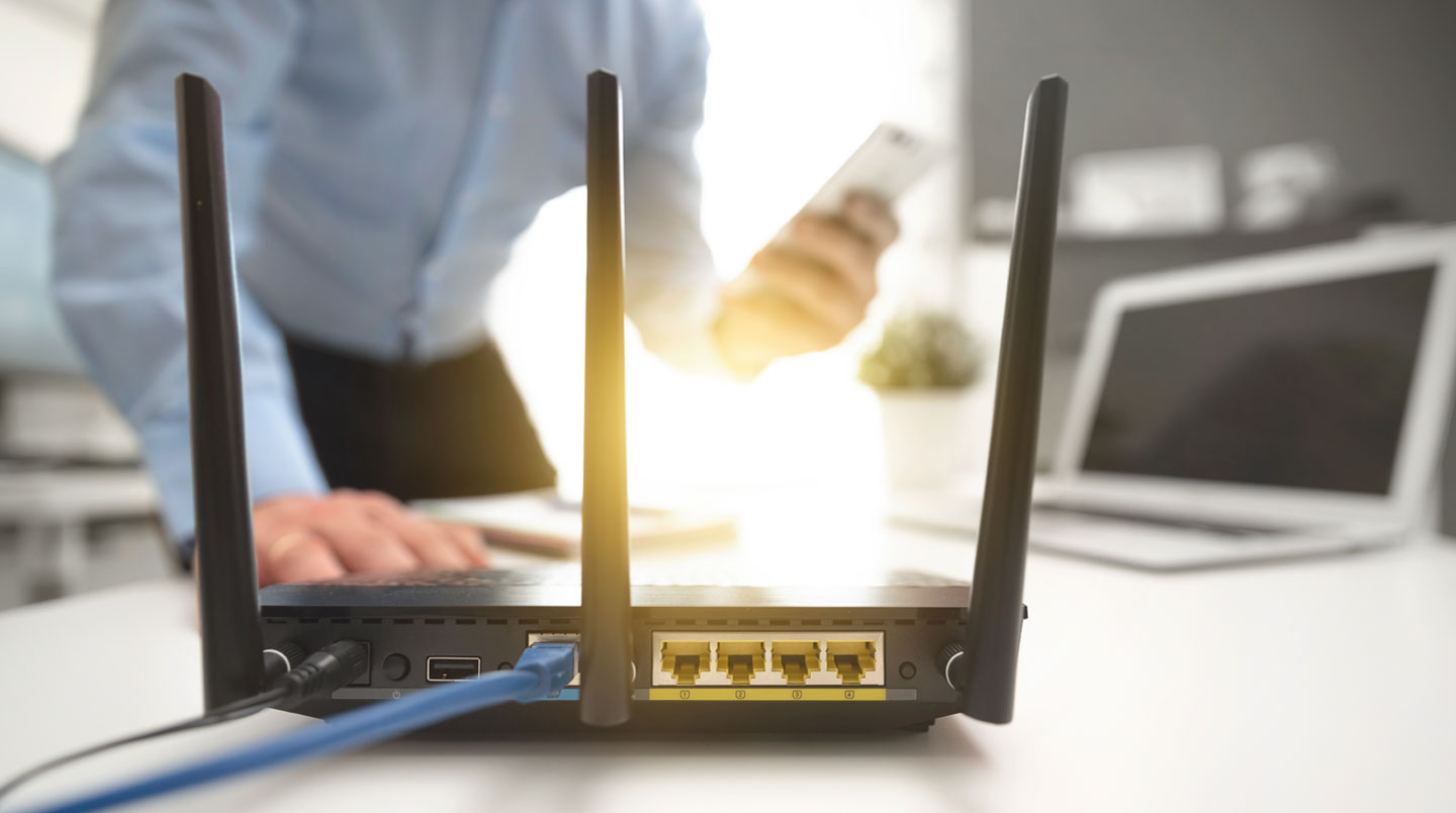 Personne travaillant sur un ordinateur portable dans un environnement de bureau épuré, avec un routeur visible sur le bureau